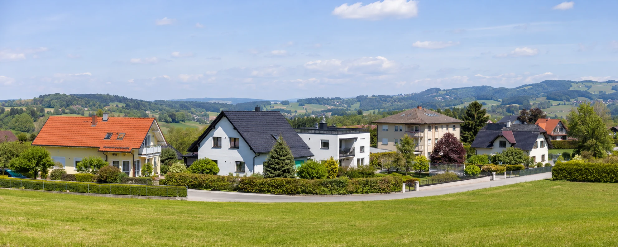 Wohnhäuser an einem österreichischen Ortsrand mit Gärten und sanften Hügeln